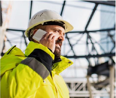 A man with a hgh vis jacket and hard hat on a mobile phone - Hero Image for the blog: RIDDOR Reporting - Making Sure Your Employees are Safe and Your Business is Compliant