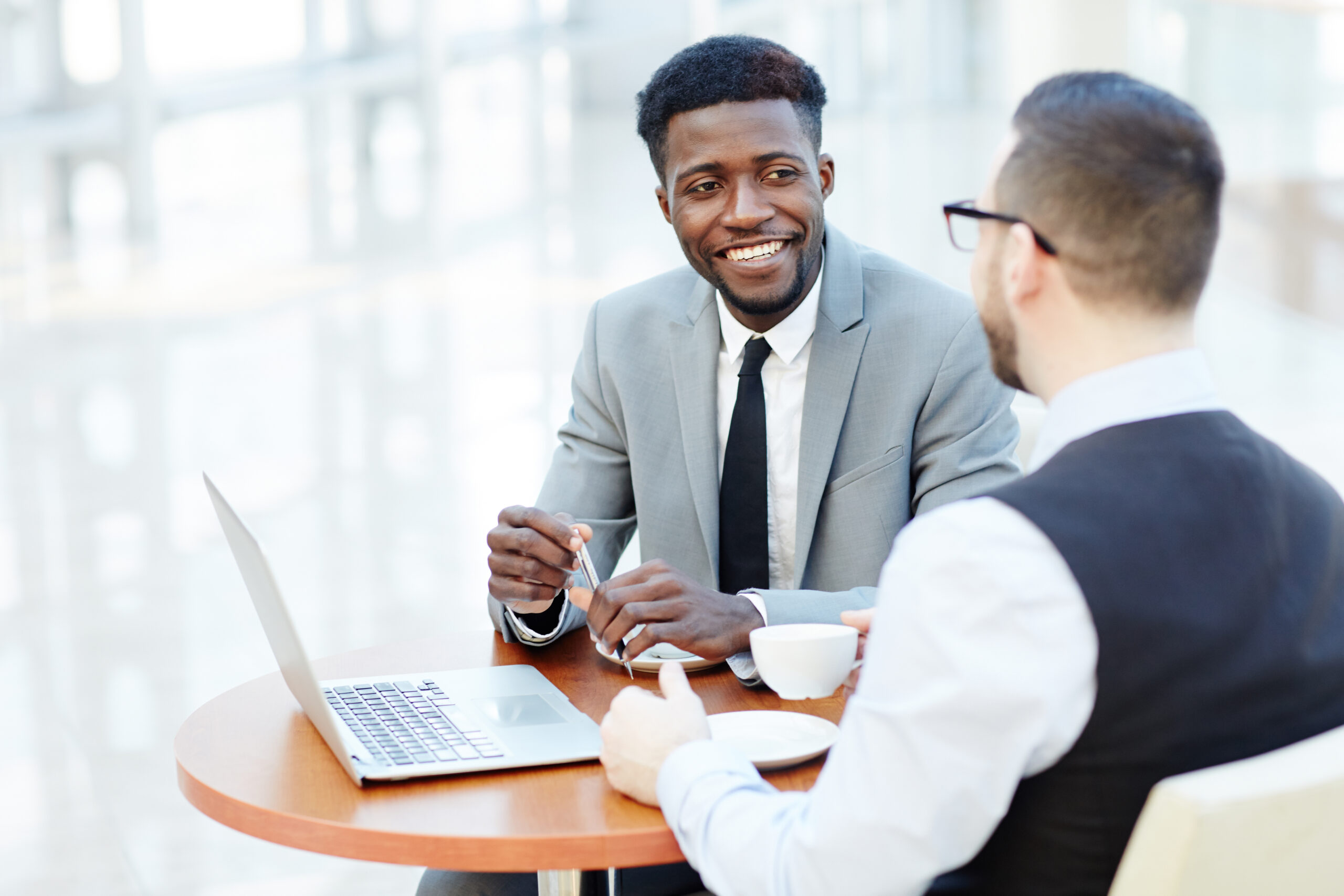 Portrait of successful African-American businessman smiling while discussing deal with Caucasian partner during meeting at coffee break to represent Benefits of Employee Wellness Programs article.