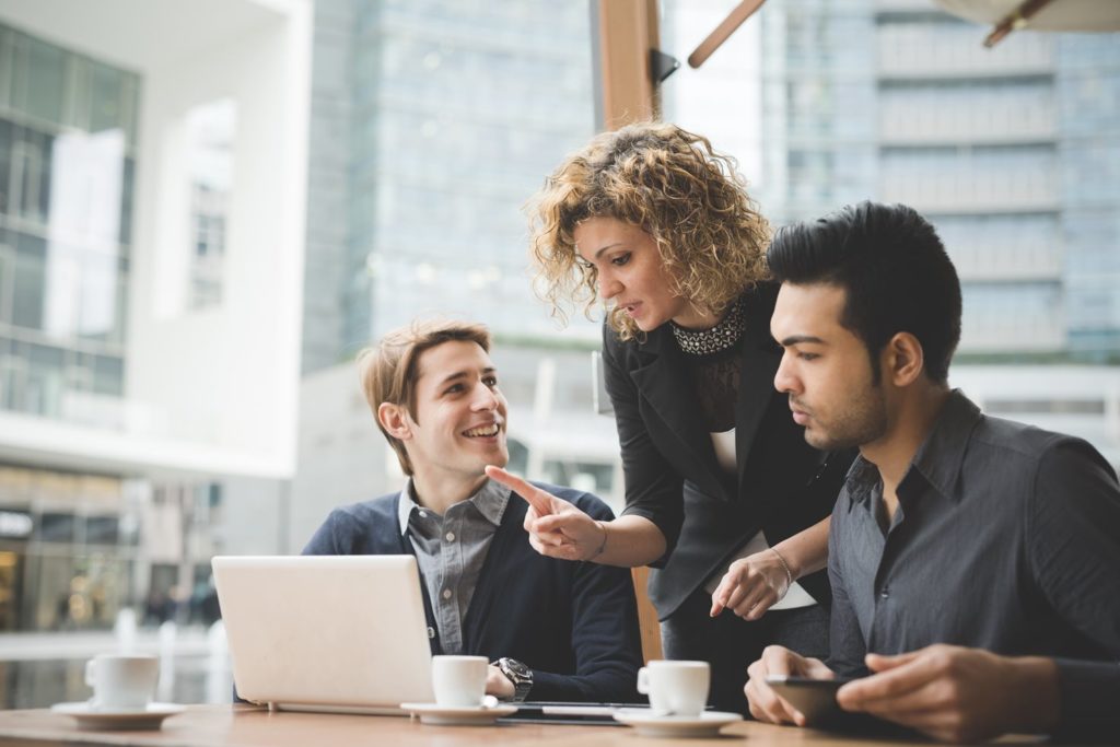 Image of a female supervisor collaborating with two men in an informal coffee setting about health and safety business partner subscriptions