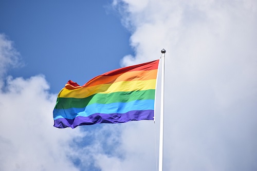Image of a pride flag (Red, Orange, Yellow, Green, Blue & Purple stripes) on a flag pole on a partially cloudy day as a hero image for Pride Month: Why is diversity, equality, and inclusion in the workplace important?